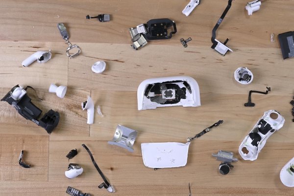 The shredded pieces of AirPods Pro 2 case and earbuds laid out on a wood table top